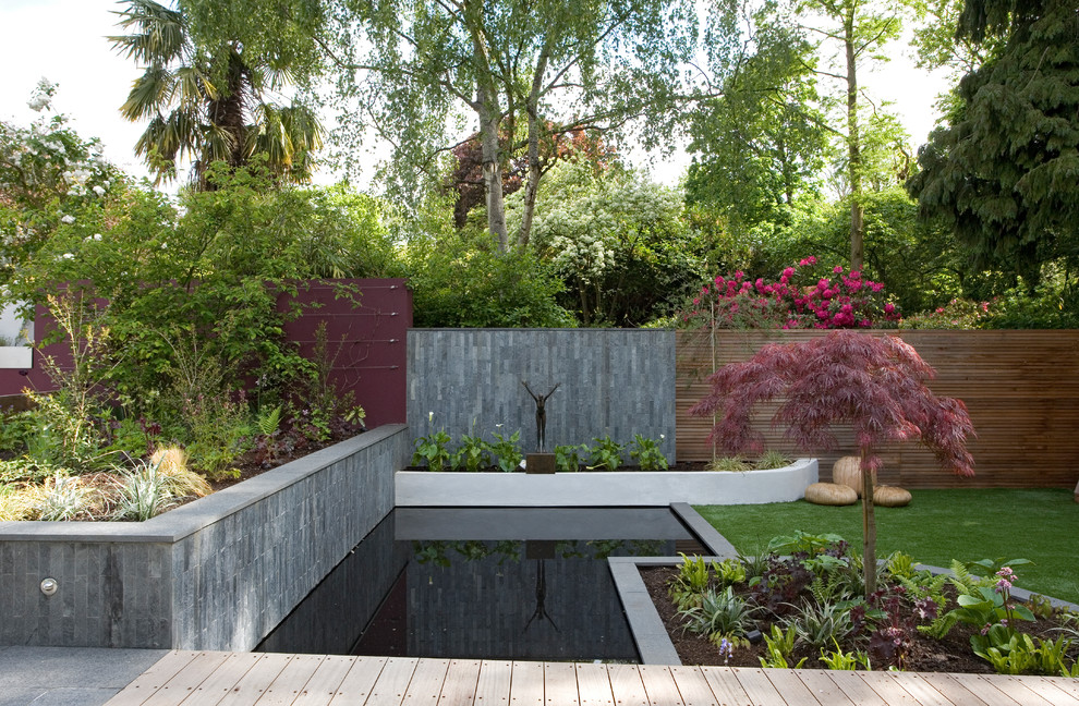 This is an example of a large contemporary backyard formal garden in London with with pond and decking.