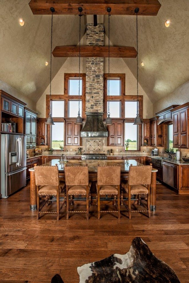This is an example of a large country u-shaped eat-in kitchen in Other with stainless steel appliances, a farmhouse sink, raised-panel cabinets, dark wood cabinets, granite benchtops, beige splashback, stone tile splashback, dark hardwood floors and with island.