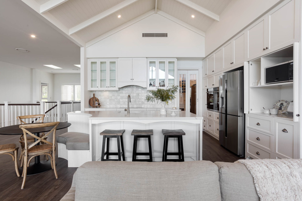 Inspiration for a large beach style l-shaped open plan kitchen in Adelaide with an undermount sink, shaker cabinets, white cabinets, quartz benchtops, metallic splashback, ceramic splashback, black appliances, laminate floors, with island, brown floor, white benchtop and vaulted.