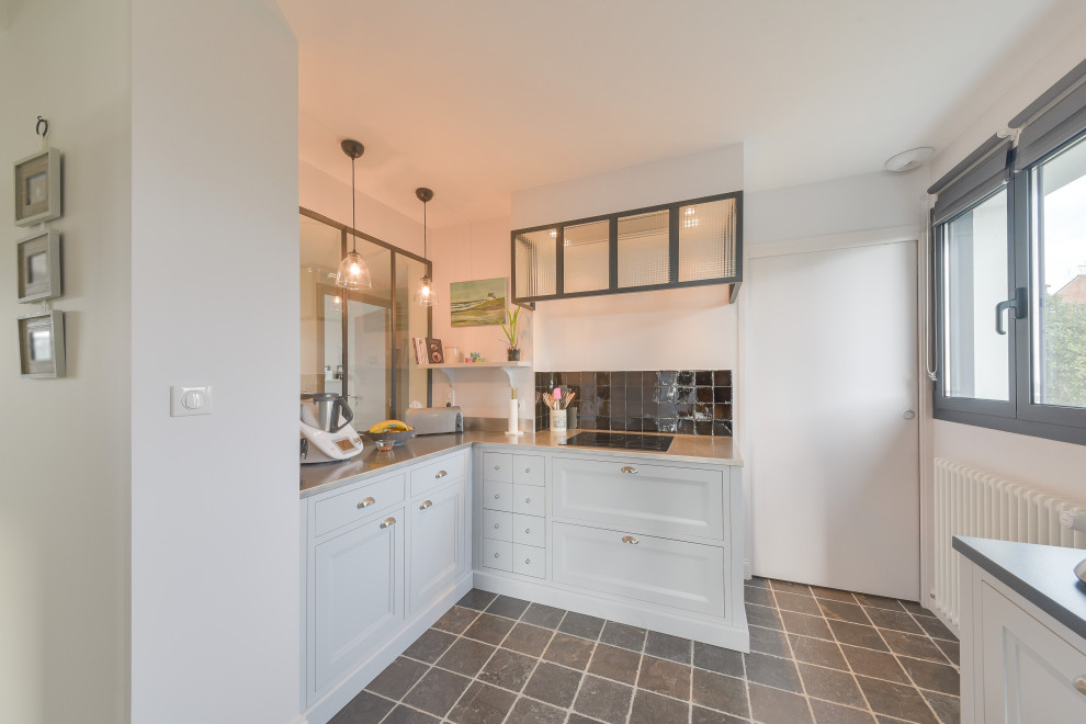 This is an example of a mid-sized beach style galley eat-in kitchen in Nantes with a double-bowl sink, recessed-panel cabinets, grey cabinets, zinc benchtops, black splashback, mosaic tile splashback, black appliances, black floor and grey benchtop.