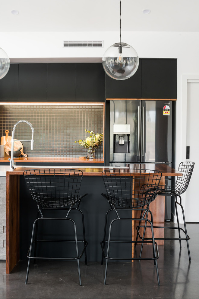 Mid-sized contemporary galley open plan kitchen in Hobart with an undermount sink, black cabinets, solid surface benchtops, black splashback, ceramic splashback, stainless steel appliances, concrete floors, with island, grey floor and white benchtop.