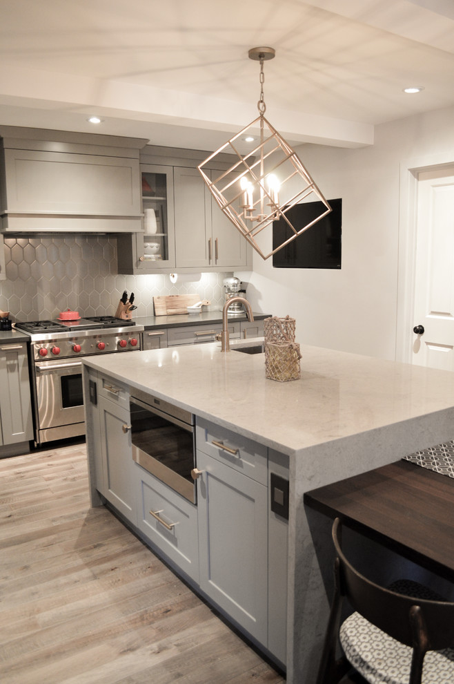 Inspiration for a mid-sized transitional l-shaped medium tone wood floor enclosed kitchen remodel in Toronto with a farmhouse sink, shaker cabinets, gray cabinets, quartz countertops, gray backsplash, porcelain backsplash, paneled appliances and an island