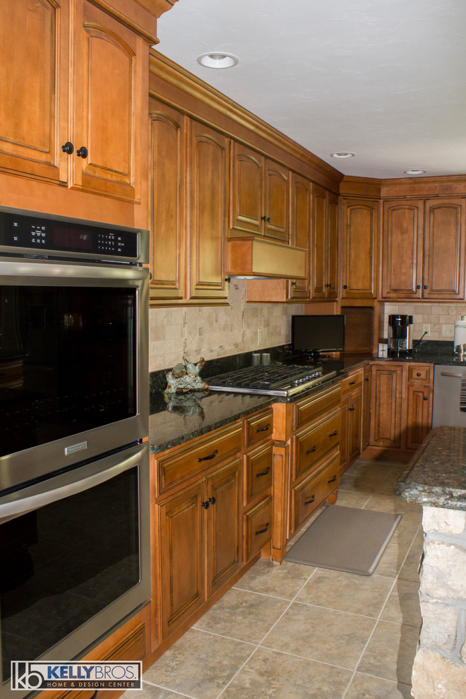 Bild på ett stort lantligt kök, med luckor med upphöjd panel, skåp i mellenmörkt trä, granitbänkskiva, beige stänkskydd, stänkskydd i stenkakel, rostfria vitvaror och en köksö