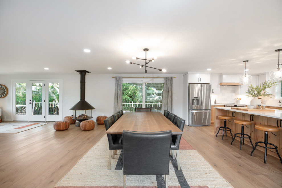 Example of a huge minimalist vinyl floor and beige floor kitchen/dining room combo design in Portland with white walls, a wood stove and a metal fireplace
