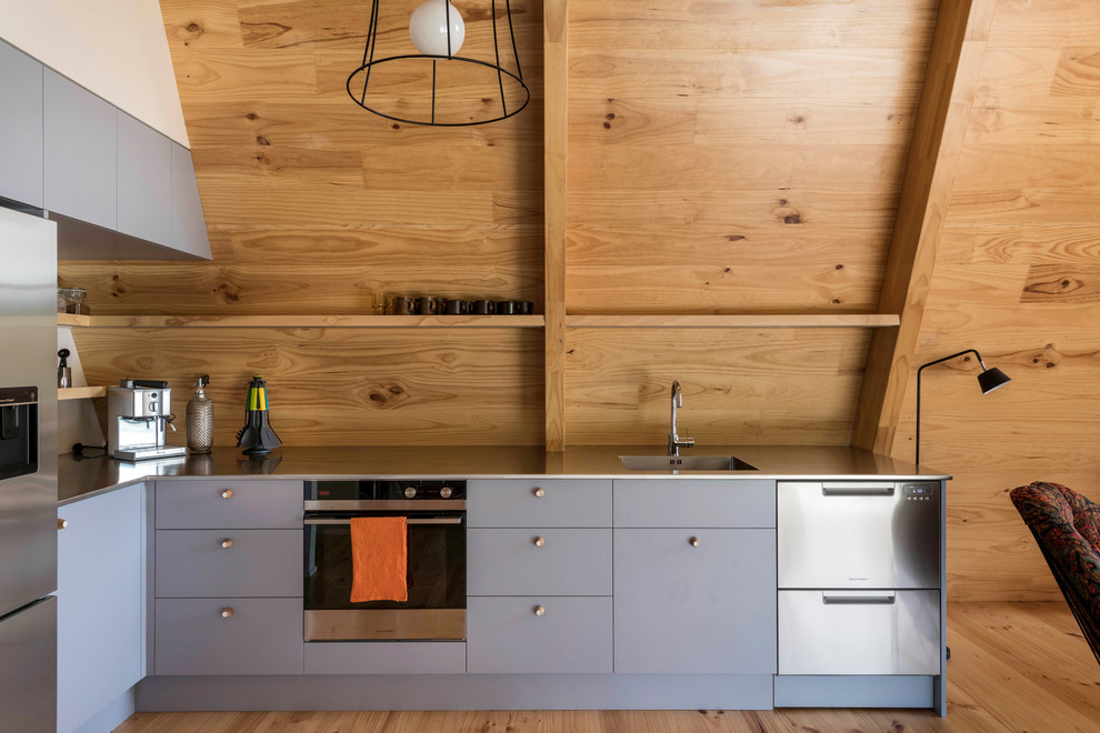 This is an example of a contemporary l-shaped open plan kitchen in Christchurch with an integrated sink, flat-panel cabinets, grey cabinets, stainless steel benchtops, beige splashback, timber splashback, stainless steel appliances, medium hardwood floors, no island, beige floor and grey benchtop.