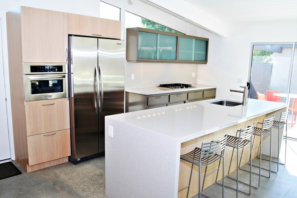 Mid-sized midcentury l-shaped eat-in kitchen in Los Angeles with an undermount sink, flat-panel cabinets, medium wood cabinets, quartz benchtops, yellow splashback, white appliances, concrete floors and multiple islands.