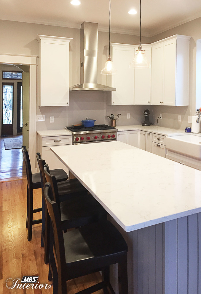 Mid-sized transitional l-shaped eat-in kitchen in Cincinnati with a farmhouse sink, shaker cabinets, white cabinets, quartz benchtops, grey splashback, stainless steel appliances, light hardwood floors, with island and beige floor.