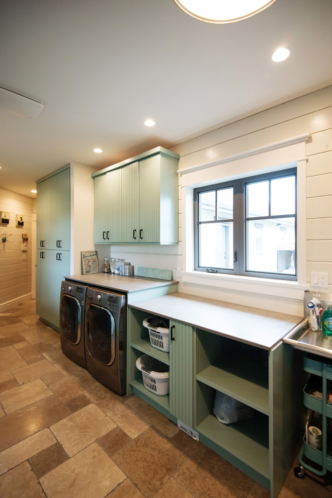 This is an example of a large country single-wall dedicated laundry room in Vancouver with louvered cabinets, blue cabinets, concrete benchtops, white walls, travertine floors, a side-by-side washer and dryer and beige floor.