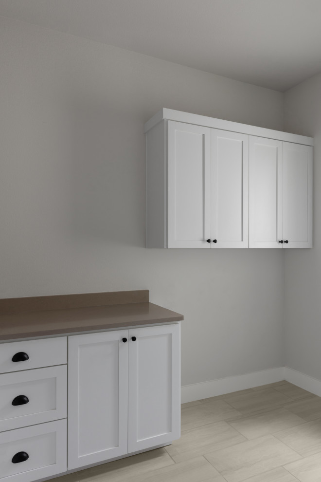 Photo of a mid-sized transitional l-shaped dedicated laundry room in Austin with recessed-panel cabinets, white cabinets, quartz benchtops, beige walls, ceramic floors, a side-by-side washer and dryer, brown floor and grey benchtop.