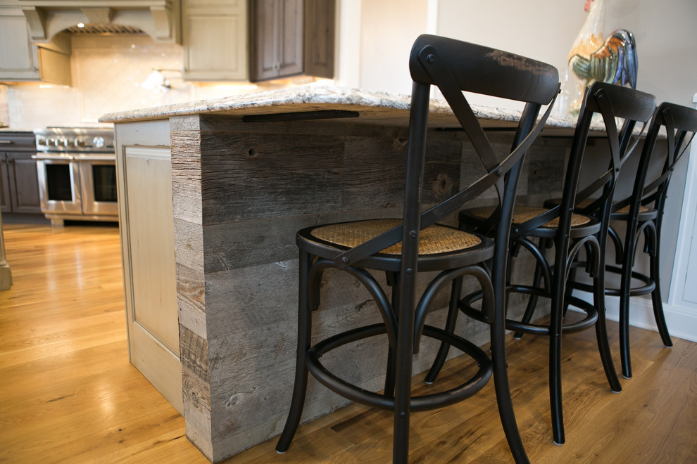 Large transitional u-shaped medium tone wood floor and brown floor kitchen photo in Indianapolis with a farmhouse sink, raised-panel cabinets, dark wood cabinets, granite countertops, white backsplash, subway tile backsplash, paneled appliances, an island and multicolored countertops