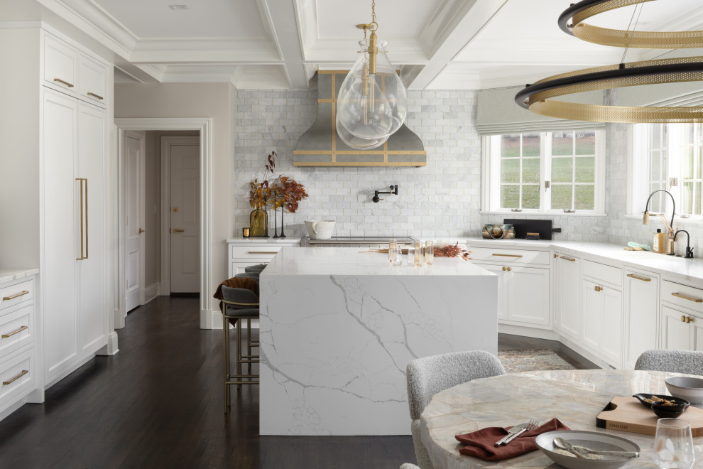 Foto på ett stort vintage vit kök, med en undermonterad diskho, skåp i shakerstil, vita skåp, bänkskiva i kvarts, grått stänkskydd, stänkskydd i marmor, integrerade vitvaror, mörkt trägolv, en köksö och brunt golv