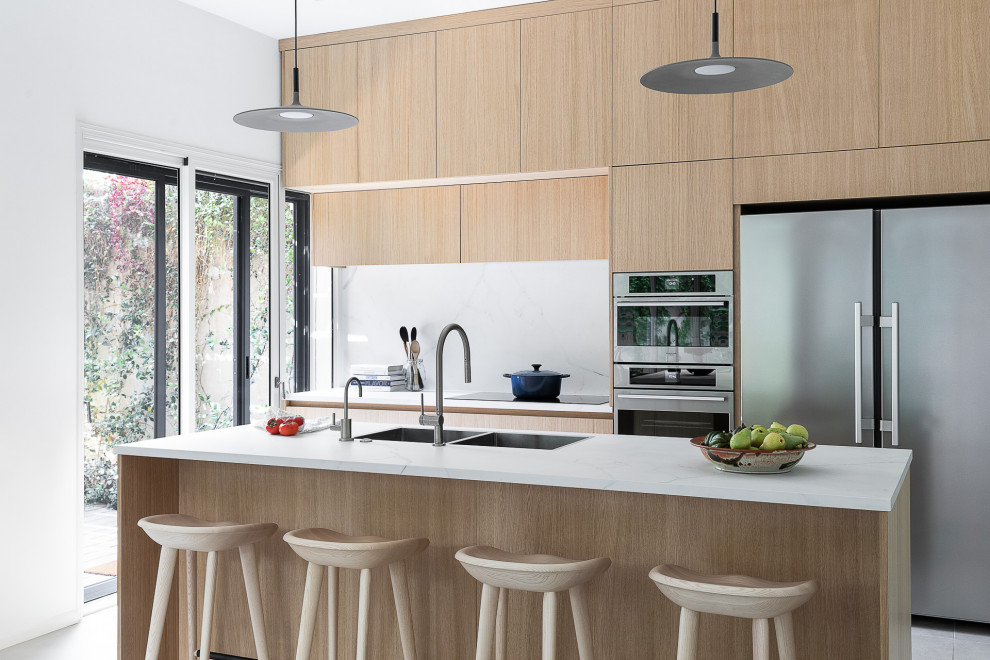 This is an example of a contemporary eat-in kitchen in Tel Aviv with a double-bowl sink, flat-panel cabinets, light wood cabinets, quartzite benchtops, white splashback, stone slab splashback, stainless steel appliances, porcelain floors, with island, grey floor and white benchtop.