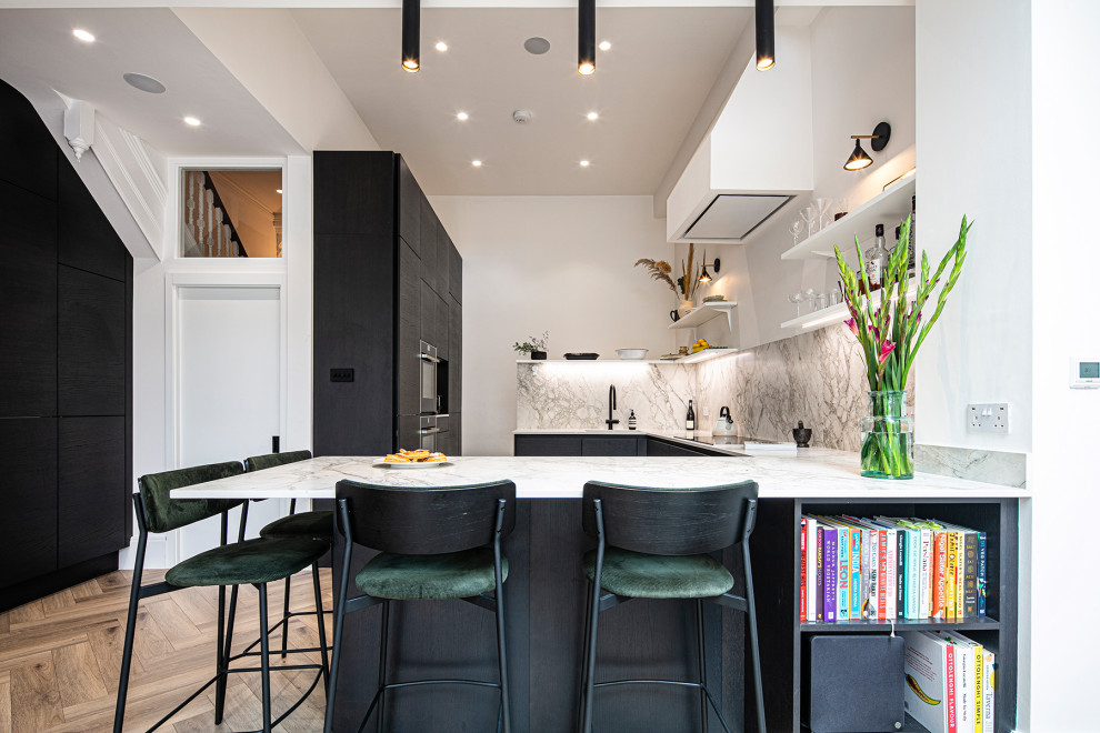 Photo of a mid-sized contemporary u-shaped eat-in kitchen in London with a single-bowl sink, flat-panel cabinets, black cabinets, quartz benchtops, white splashback, engineered quartz splashback, panelled appliances, laminate floors, a peninsula, brown floor and white benchtop.
