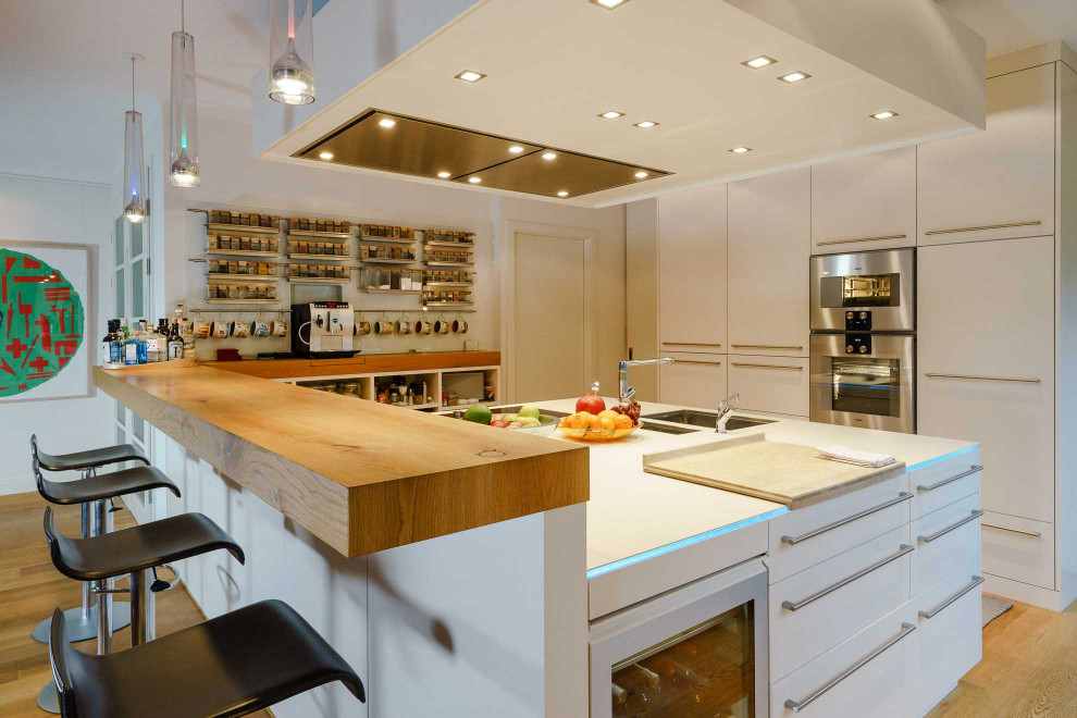 This is an example of a large modern open plan kitchen in Hamburg with an undermount sink, flat-panel cabinets, white cabinets, glass sheet splashback, medium hardwood floors, white benchtop and wallpaper.