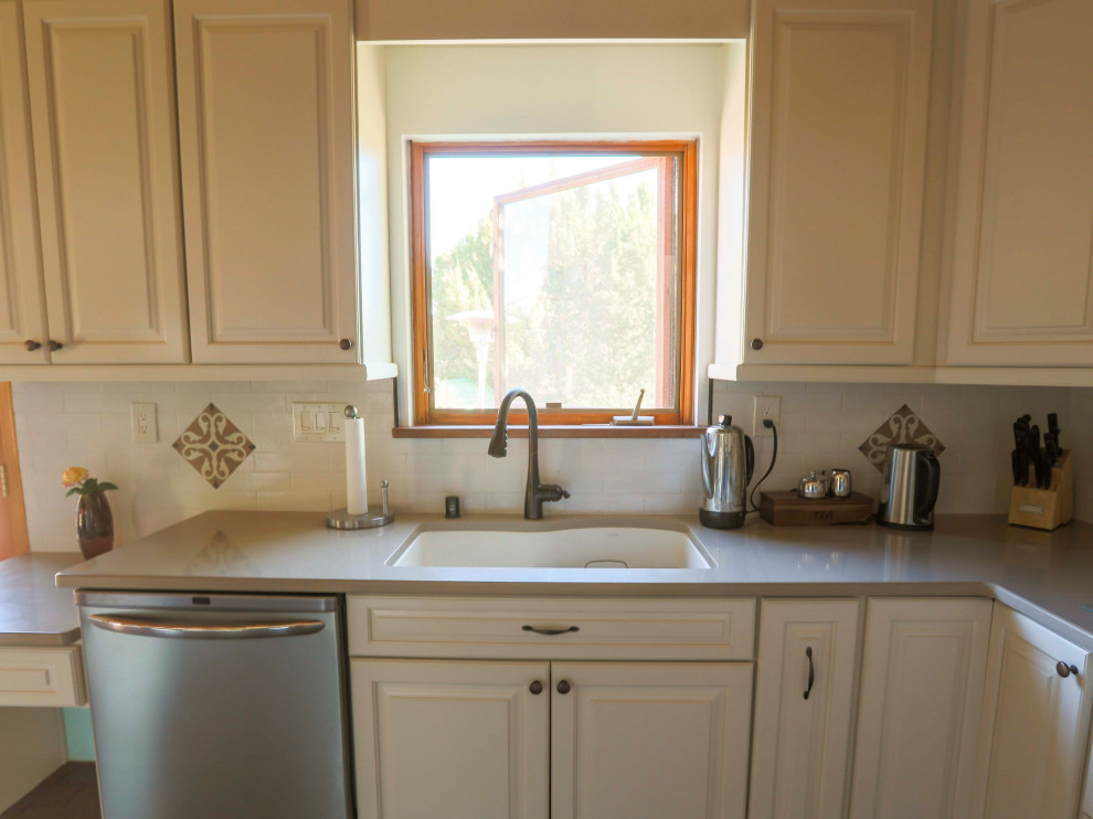 Inspiration for a mid-sized transitional l-shaped eat-in kitchen in Albuquerque with an undermount sink, raised-panel cabinets, white cabinets, quartz benchtops, white splashback, porcelain splashback, stainless steel appliances, brick floors, a peninsula, brown floor and grey benchtop.