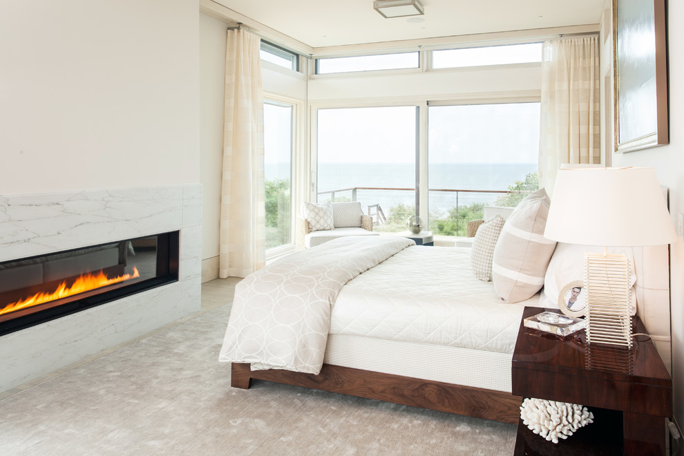 This is an example of a large contemporary master bedroom in Boston with white walls, a ribbon fireplace, bamboo floors, beige floor and a stone fireplace surround.