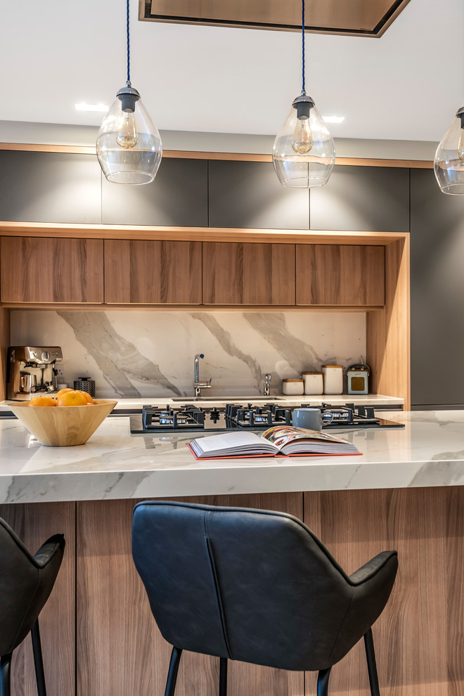 Photo of a contemporary single-wall open plan kitchen in Hertfordshire with flat-panel cabinets, grey cabinets, white splashback, light hardwood floors, with island, beige floor and white benchtop.
