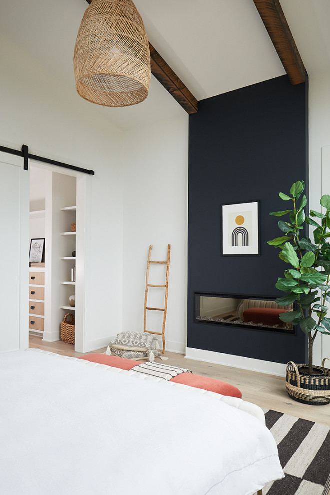 Foto de dormitorio principal contemporáneo de tamaño medio con paredes blancas, suelo de madera clara, chimenea lineal, marco de chimenea de madera y vigas vistas