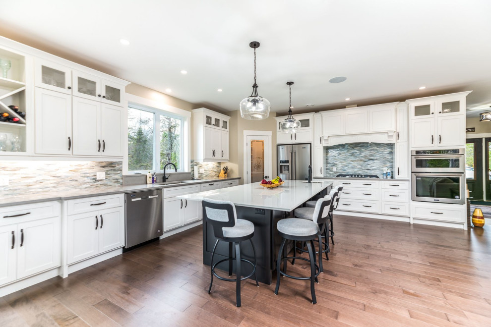 Mid-sized transitional medium tone wood floor and brown floor open concept kitchen photo with an undermount sink, shaker cabinets, white cabinets, granite countertops, gray backsplash, mosaic tile backsplash, stainless steel appliances, an island and gray countertops