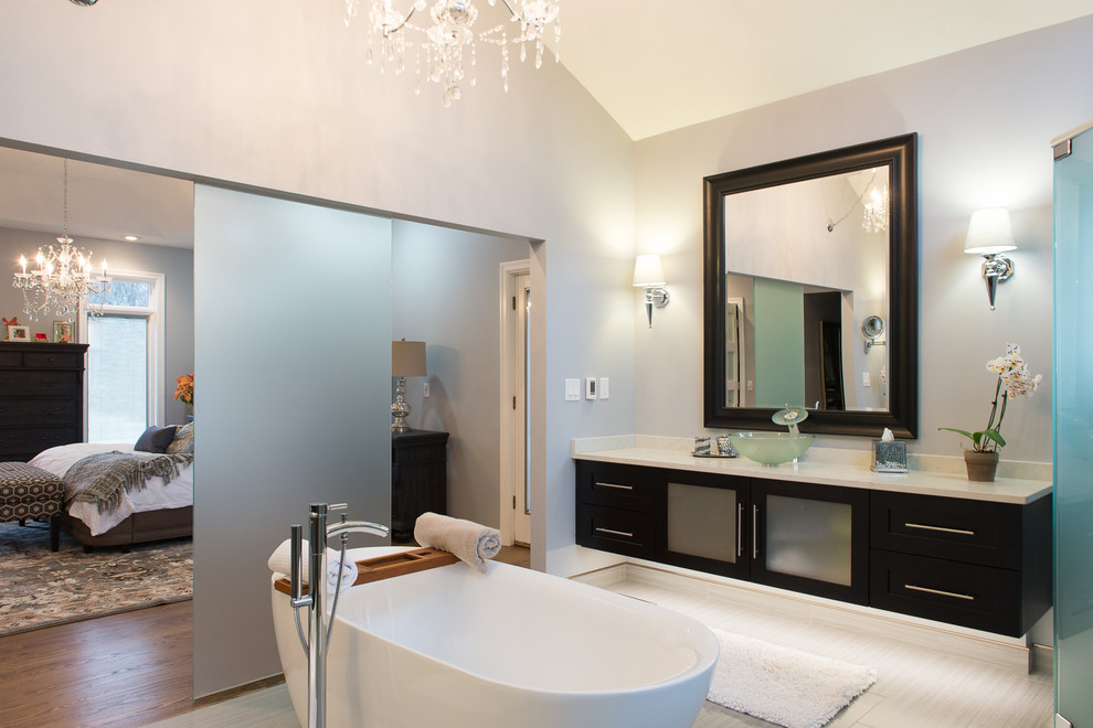 Large contemporary master bathroom in Detroit with glass-front cabinets, dark wood cabinets, a freestanding tub, a double shower, a bidet, gray tile, pebble tile, grey walls, porcelain floors, a vessel sink and engineered quartz benchtops.