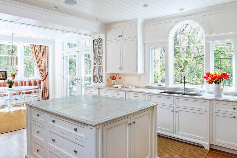 Large traditional l-shaped eat-in kitchen in DC Metro with an undermount sink, beaded inset cabinets, white cabinets, limestone benchtops, white splashback, medium hardwood floors and with island.