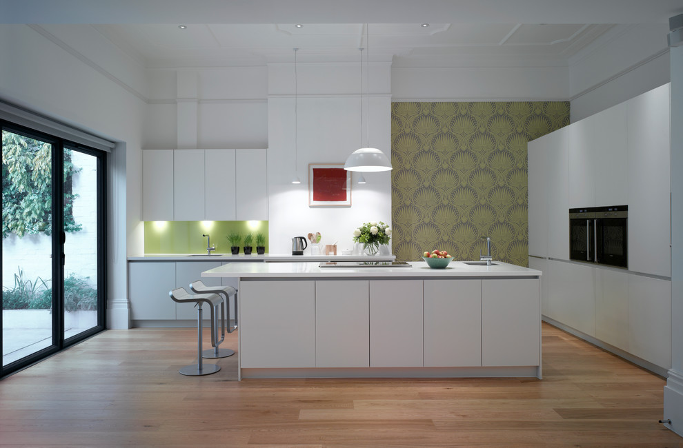 Design ideas for a large contemporary open plan kitchen in London with an undermount sink, flat-panel cabinets, white cabinets, solid surface benchtops, glass sheet splashback and with island.