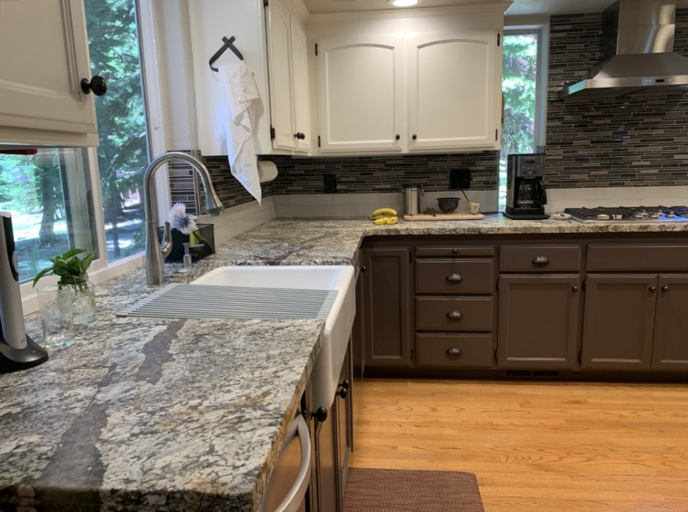 Mid-sized transitional u-shaped light wood floor and yellow floor eat-in kitchen photo with a farmhouse sink, recessed-panel cabinets, brown cabinets, granite countertops, multicolored backsplash, glass sheet backsplash, stainless steel appliances, an island and multicolored countertops