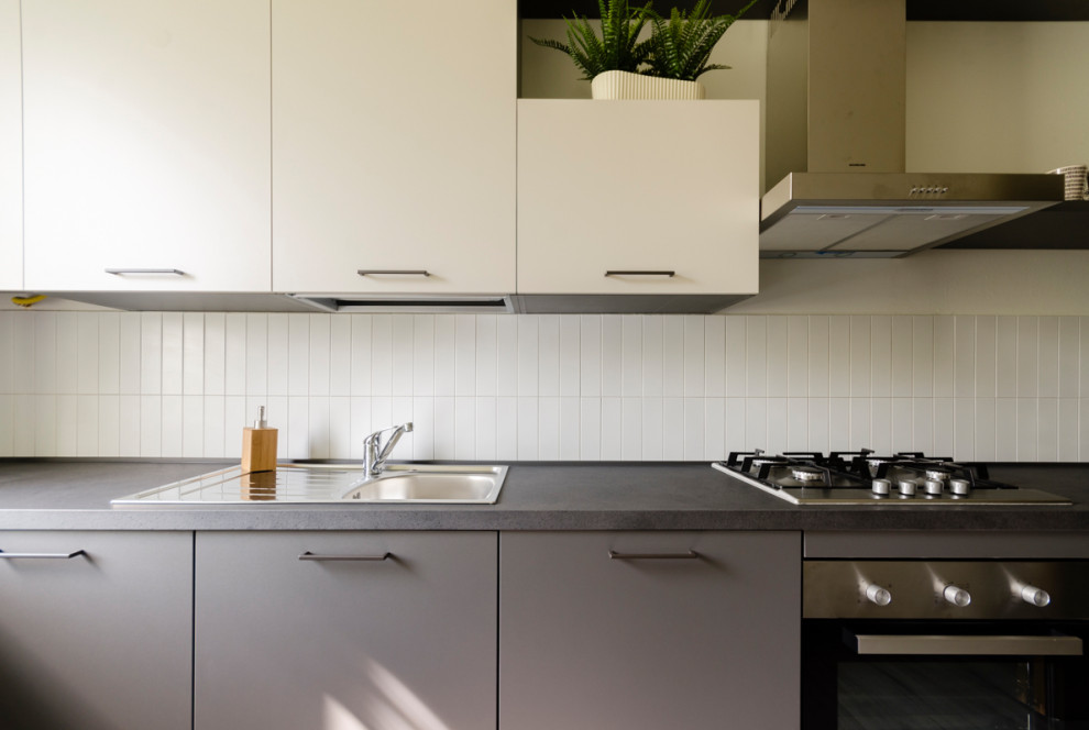 This is an example of a small modern single-wall separate kitchen in Milan with a single-bowl sink, flat-panel cabinets, beige cabinets, laminate benchtops, white splashback, matchstick tile splashback, stainless steel appliances, laminate floors, grey floor and grey benchtop.