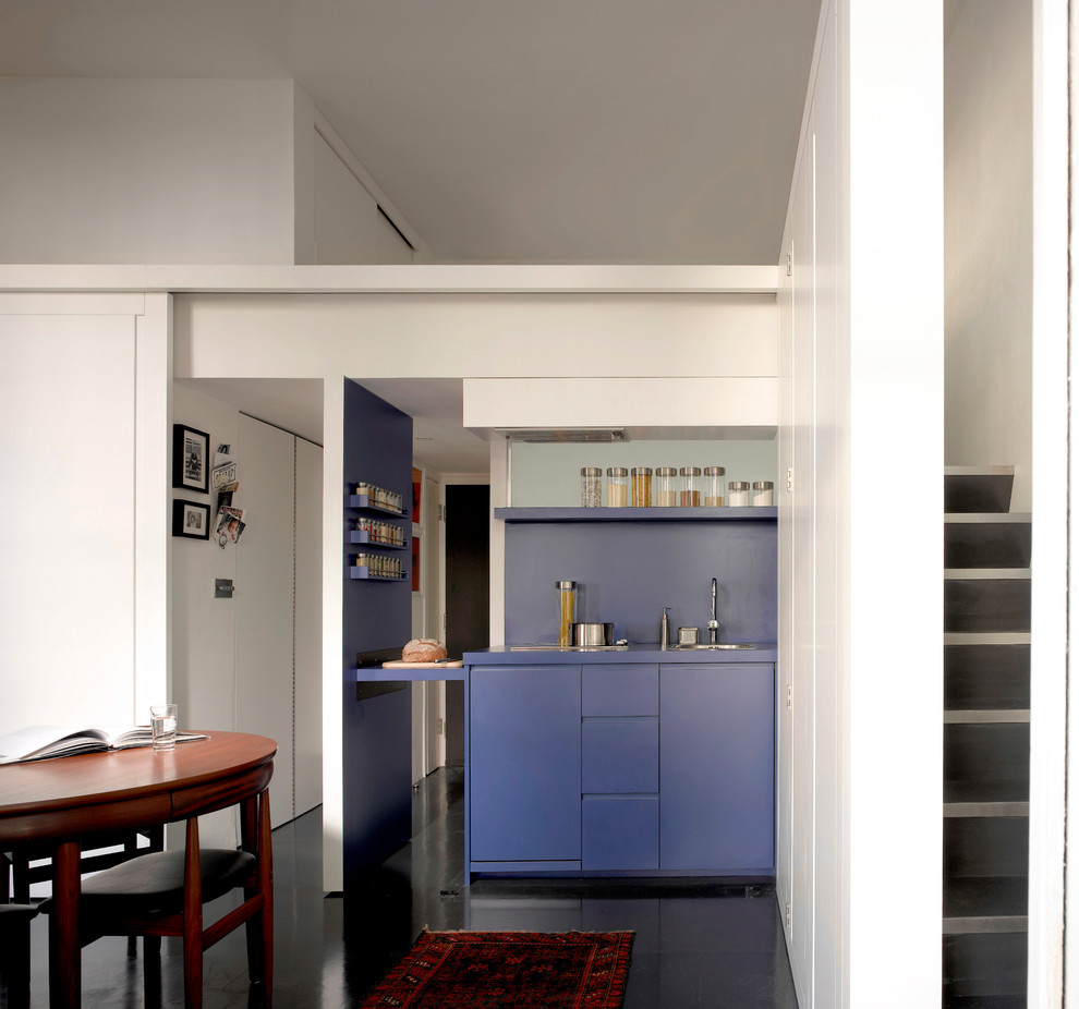 This is an example of a small contemporary open plan kitchen in London with a drop-in sink, flat-panel cabinets, blue cabinets, stainless steel appliances, ceramic floors and blue splashback.