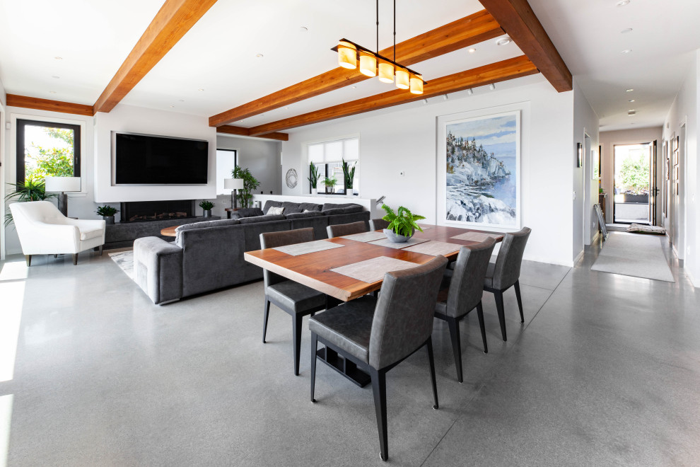 Exemple d'une grande salle à manger ouverte sur la cuisine tendance avec un mur blanc, sol en béton ciré, une cheminée standard, un manteau de cheminée en béton, un sol gris et poutres apparentes.
