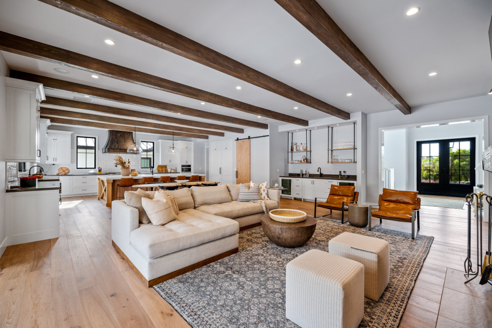 Example of a huge farmhouse open concept light wood floor, beige floor and exposed beam living room design in Los Angeles with white walls, a standard fireplace, a stone fireplace and a wall-mounted tv