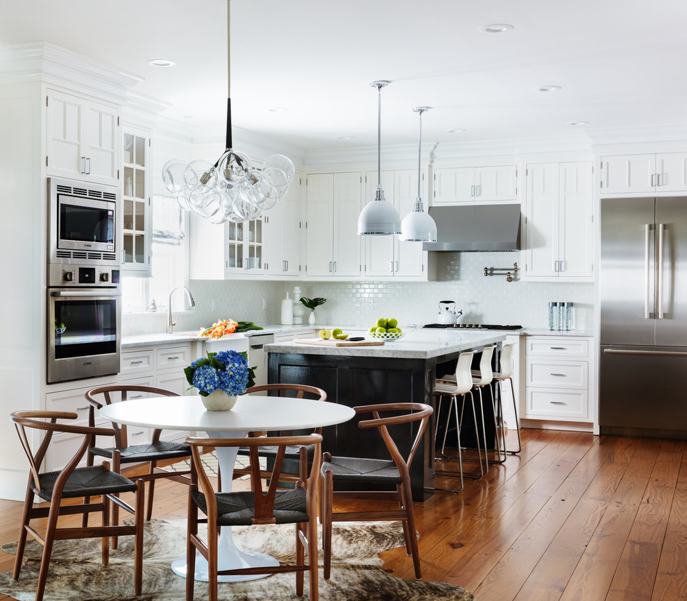 Design ideas for a large transitional l-shaped eat-in kitchen in New York with marble benchtops, stainless steel appliances, medium hardwood floors, with island, a farmhouse sink, recessed-panel cabinets, white cabinets, white splashback, brown floor and grey benchtop.