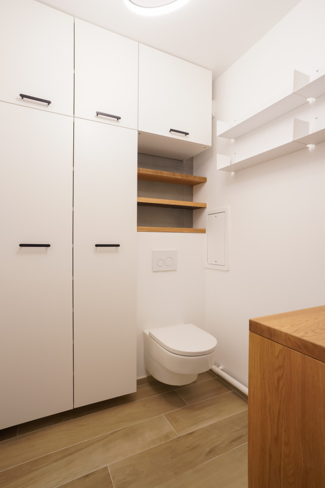 Photo of a mid-sized modern powder room in Paris with flat-panel cabinets, white cabinets, a wall-mount toilet, gray tile, ceramic tile, white walls, ceramic floors, wood benchtops, beige floor, white benchtops and a floating vanity.