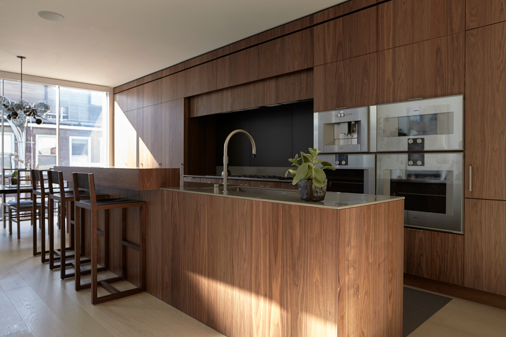 This is an example of a large modern galley eat-in kitchen in New York with an undermount sink, flat-panel cabinets, dark wood cabinets, solid surface benchtops, black splashback, stainless steel appliances, light hardwood floors and with island.