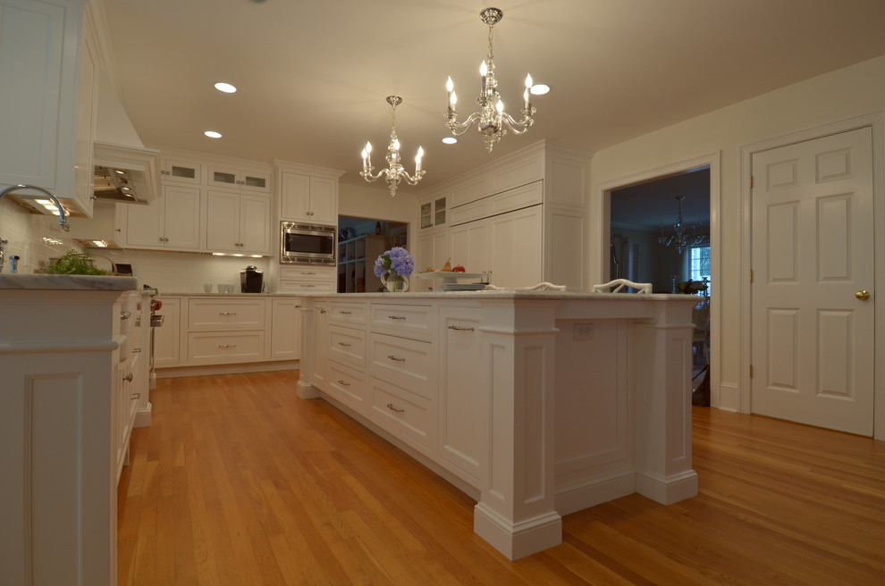 Transitional u-shaped medium tone wood floor eat-in kitchen photo in Boston with a farmhouse sink, beaded inset cabinets, white cabinets, marble countertops, white backsplash, subway tile backsplash, stainless steel appliances and an island