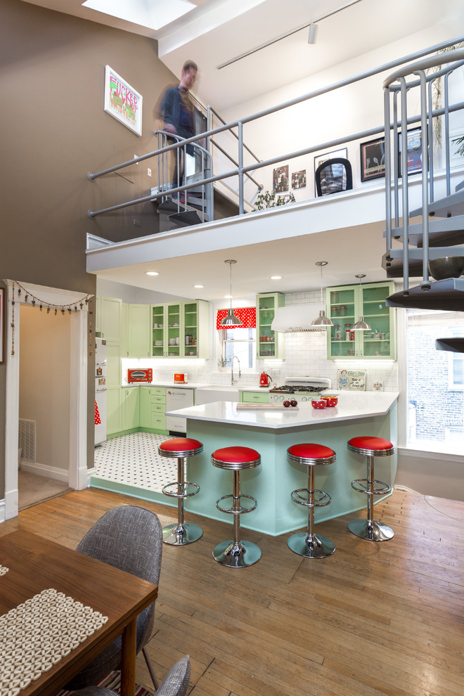This is an example of a mid-sized traditional l-shaped open plan kitchen in Chicago with a farmhouse sink, shaker cabinets, green cabinets, quartz benchtops, white splashback, subway tile splashback, white appliances, porcelain floors and a peninsula.