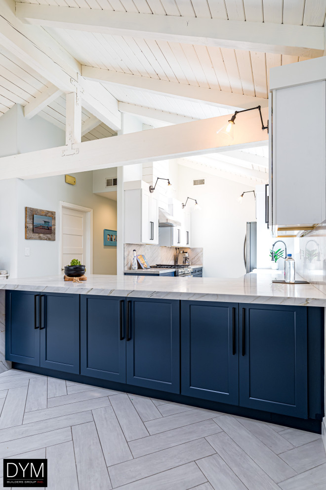 Design ideas for a coastal galley kitchen/diner in Los Angeles with a belfast sink, shaker cabinets, blue cabinets, engineered stone countertops, white splashback, engineered quartz splashback, stainless steel appliances, a breakfast bar, white floors, white worktops, a vaulted ceiling and light hardwood flooring.