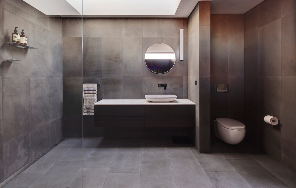 This is an example of a contemporary bathroom in Sydney with gray tile, grey walls, a vessel sink, furniture-like cabinets, dark wood cabinets, marble benchtops, an open shower, a wall-mount toilet and stone tile.