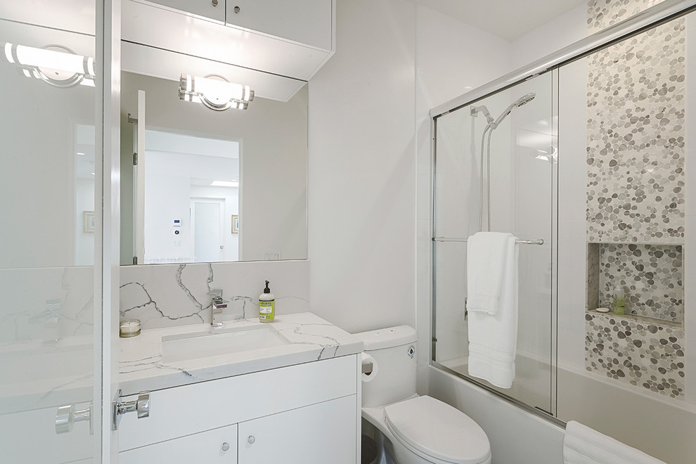 Inspiration for a small modern master bathroom in Los Angeles with flat-panel cabinets, white cabinets, an alcove tub, a shower/bathtub combo, a one-piece toilet, pebble tile, white walls, an undermount sink, engineered quartz benchtops, a sliding shower screen, a single vanity and a built-in vanity.