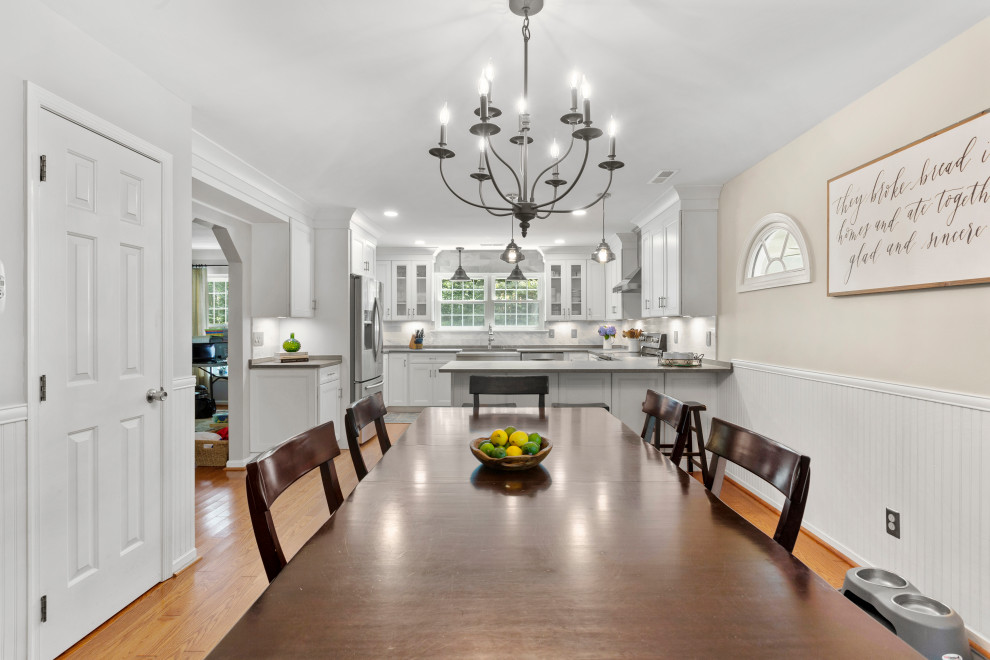 Inspiration for a mid-sized traditional u-shaped eat-in kitchen in DC Metro with a farmhouse sink, recessed-panel cabinets, white cabinets, granite benchtops, white splashback, stone tile splashback, stainless steel appliances, medium hardwood floors, no island, brown floor and grey benchtop.