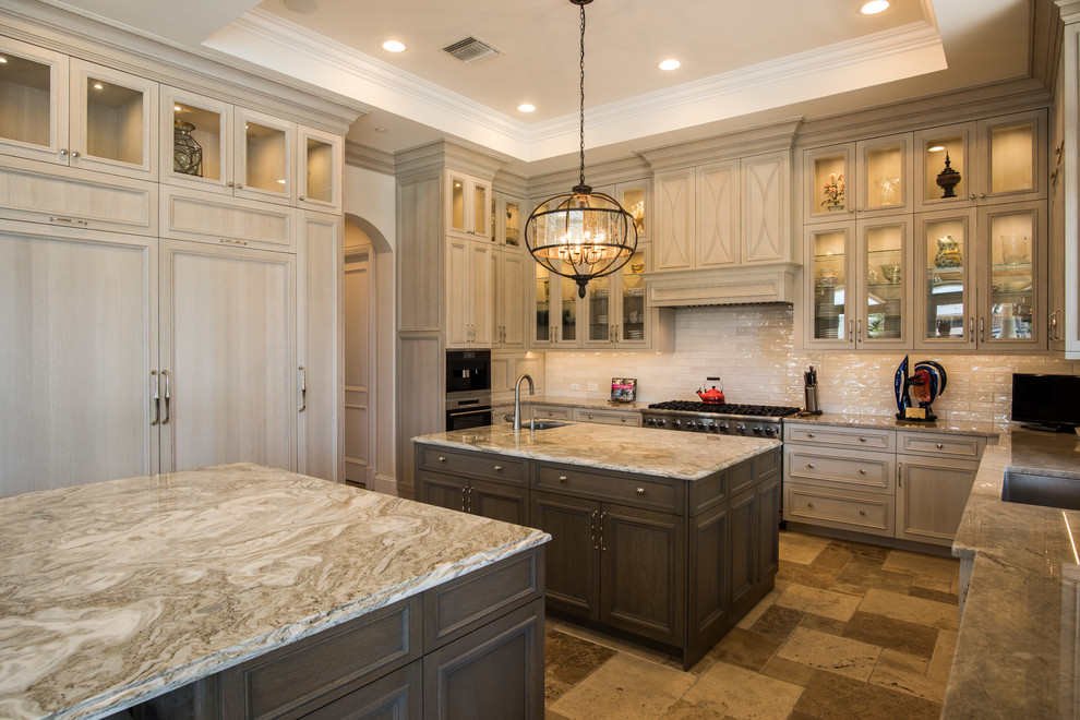 Large transitional u-shaped travertine floor and beige floor kitchen photo with an undermount sink, raised-panel cabinets, brown cabinets, quartzite countertops, white backsplash, subway tile backsplash, paneled appliances and two islands
