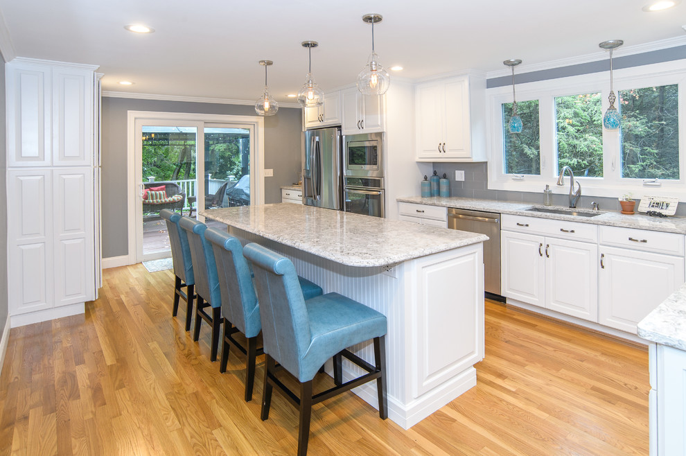 Example of a large transitional galley light wood floor kitchen pantry design in Bridgeport with a single-bowl sink, raised-panel cabinets, white cabinets, gray backsplash, ceramic backsplash, stainless steel appliances and an island