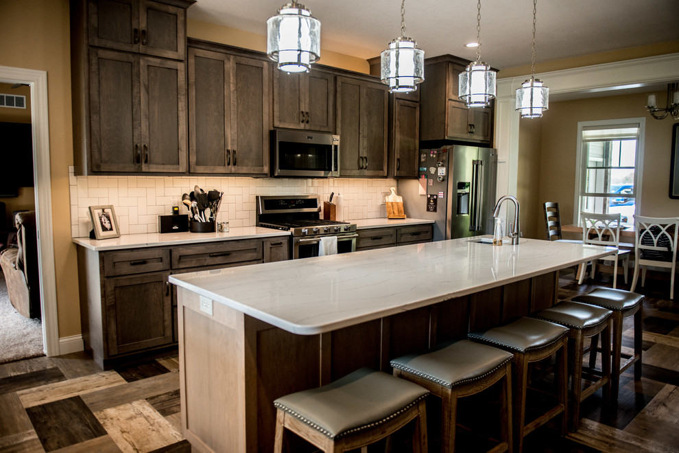 Large transitional l-shaped vinyl floor and multicolored floor open concept kitchen photo with a farmhouse sink, shaker cabinets, gray cabinets, quartz countertops, white backsplash, subway tile backsplash, stainless steel appliances, an island and white countertops