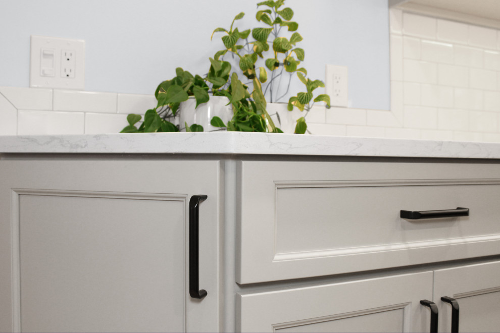 Inspiration for a large transitional u-shaped light wood floor and brown floor enclosed kitchen remodel in Boston with a double-bowl sink, shaker cabinets, gray cabinets, quartz countertops, white backsplash, porcelain backsplash, black appliances, an island and white countertops
