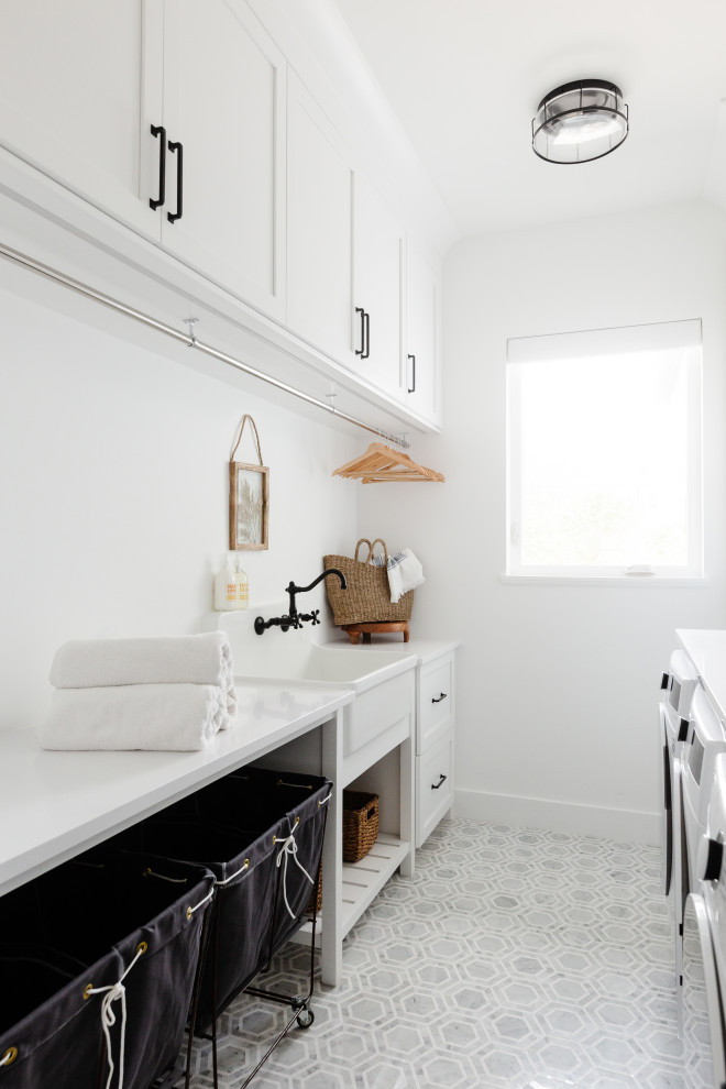 Large beach style galley utility room in Miami with a farmhouse sink, shaker cabinets, white cabinets, quartz benchtops, white splashback, stone tile splashback, white walls, marble floors, a side-by-side washer and dryer, multi-coloured floor and white benchtop.
