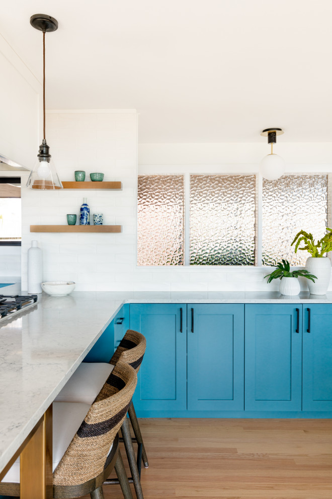 Inspiration for an eclectic kitchen in Seattle with an undermount sink, shaker cabinets, blue cabinets, quartz benchtops, white splashback, ceramic splashback, stainless steel appliances, light hardwood floors, a peninsula and white benchtop.