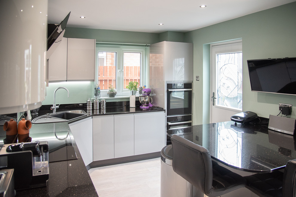 Mid-sized contemporary separate kitchen in Sussex with a drop-in sink, flat-panel cabinets, grey cabinets, granite benchtops, black splashback, black appliances, with island and black benchtop.