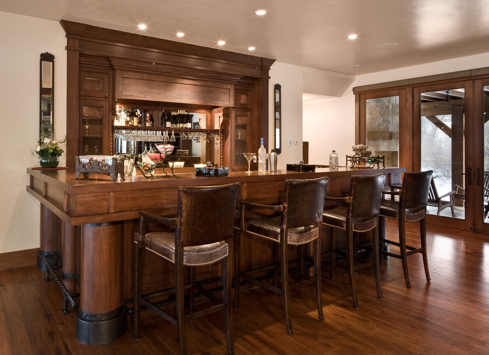 Photo of a traditional u-shaped seated home bar in Salt Lake City with dark hardwood floors, dark wood cabinets, wood benchtops, mirror splashback and brown benchtop.