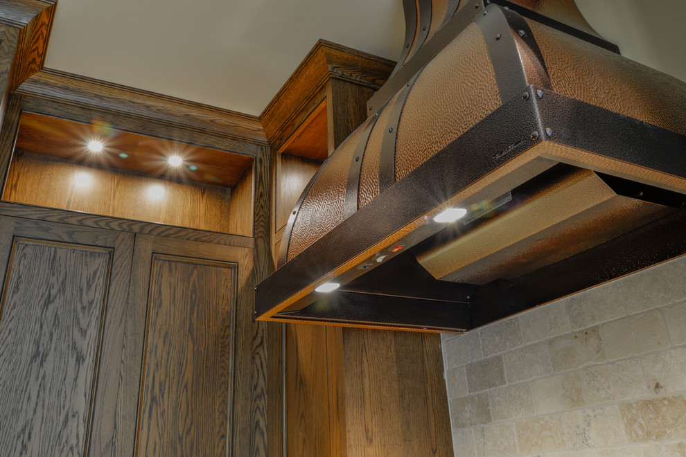 Example of a large mountain style l-shaped slate floor and gray floor enclosed kitchen design with an undermount sink, recessed-panel cabinets, dark wood cabinets, granite countertops, beige backsplash, stone tile backsplash, paneled appliances, a peninsula and brown countertops