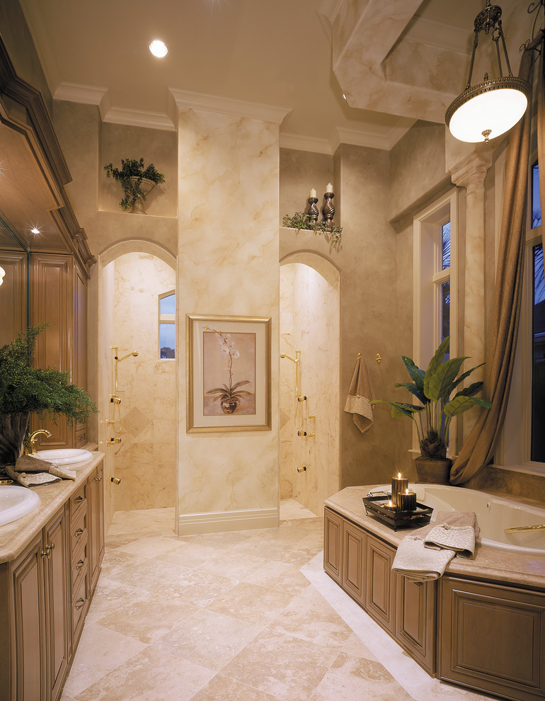 Photo of a large mediterranean master bathroom in Miami with a drop-in sink, raised-panel cabinets, medium wood cabinets, granite benchtops, a drop-in tub, an open shower, beige tile, stone tile, beige walls and travertine floors.